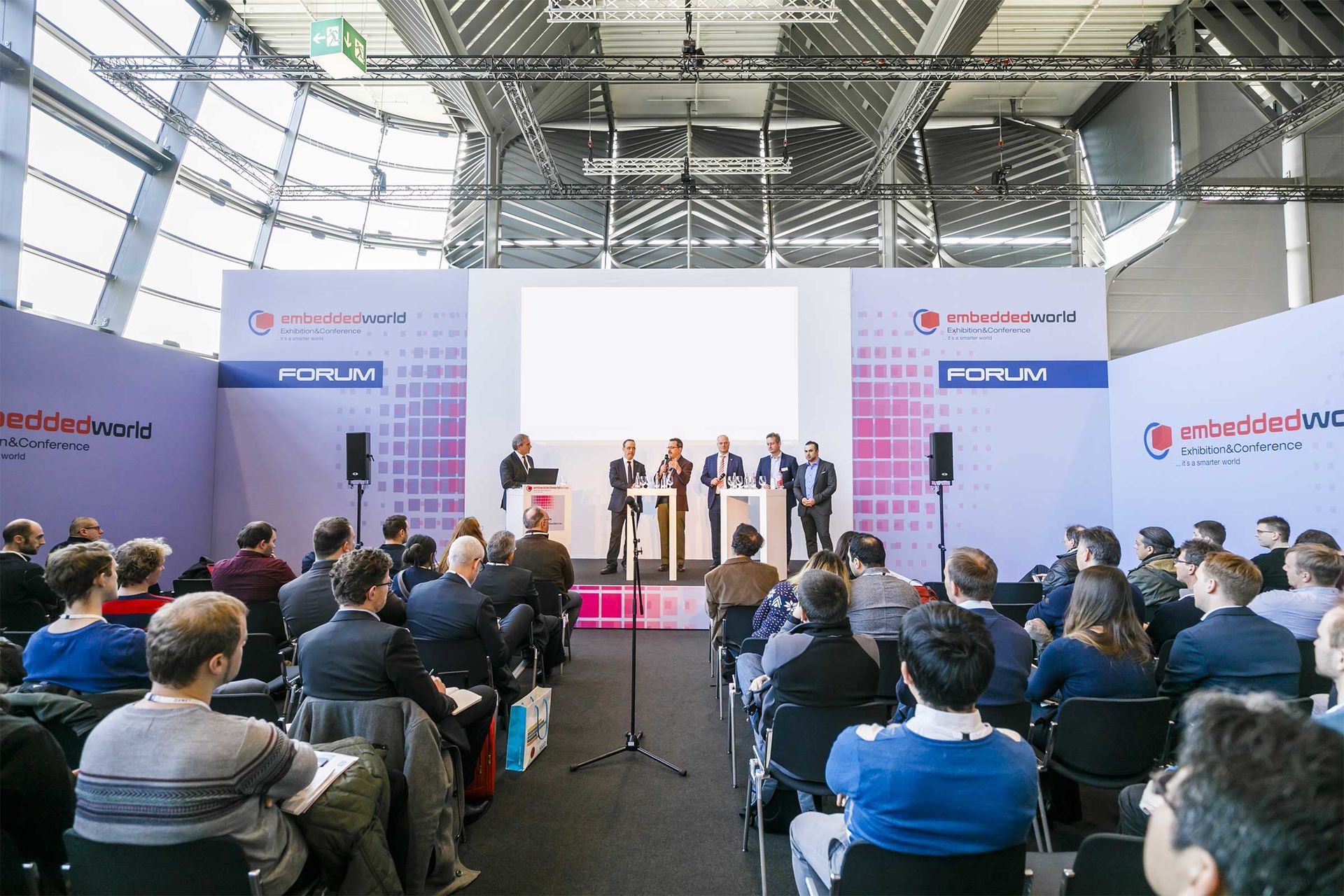 Auf dem Foto sehen Sie eine Diskussionsveranstaltung im Rahmen der embedded world Exhibition&Conference auf einem Podium diskutieren Experten vor einem großem, interessiertem Podium.
