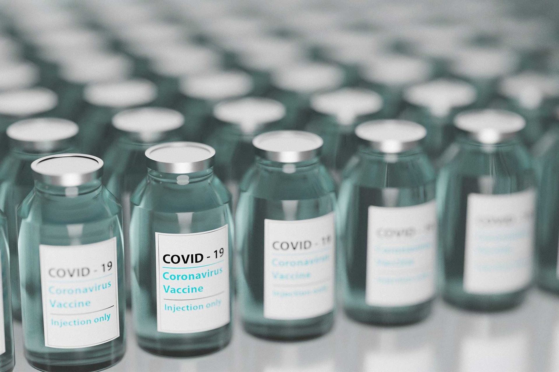 Aufgereihte Glas-Vials mit Metallverschluss. Auf den Etiketten der Glasbehälter steht auf Englisch Covid-19, Coronavirus Vaccine, Injection only