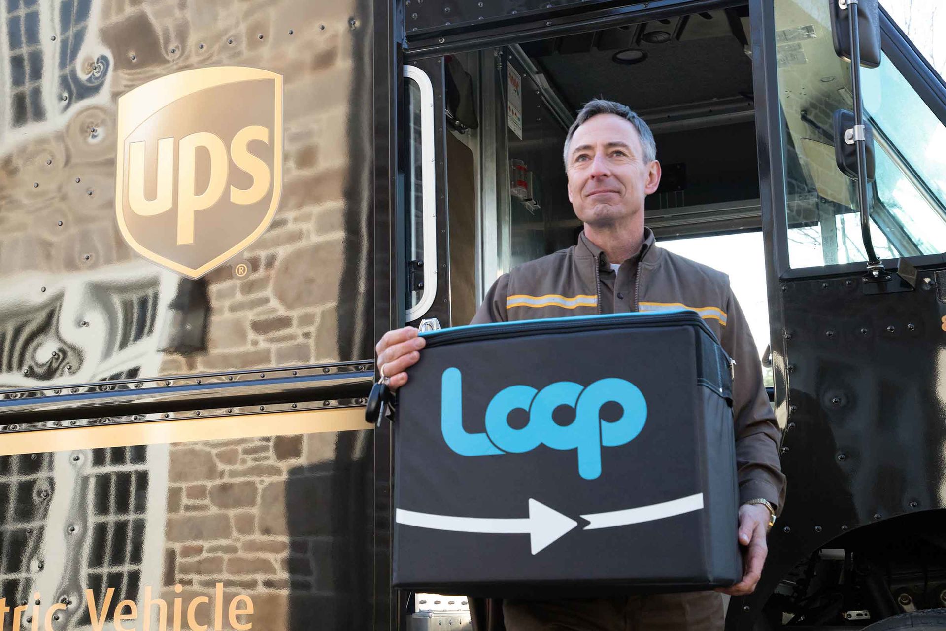 Ein Lieferfahrer von UPS steigt aus einem Lieferfahrzeug aus. Er hält eine Mehrweg-Versandbox von Loop in den Händen.