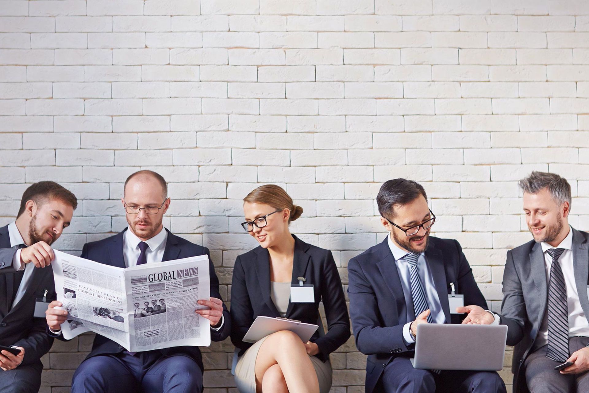 Fünf Personen sitzen in einer Reihe, lesen Zeitung und arbeiten am Laptop