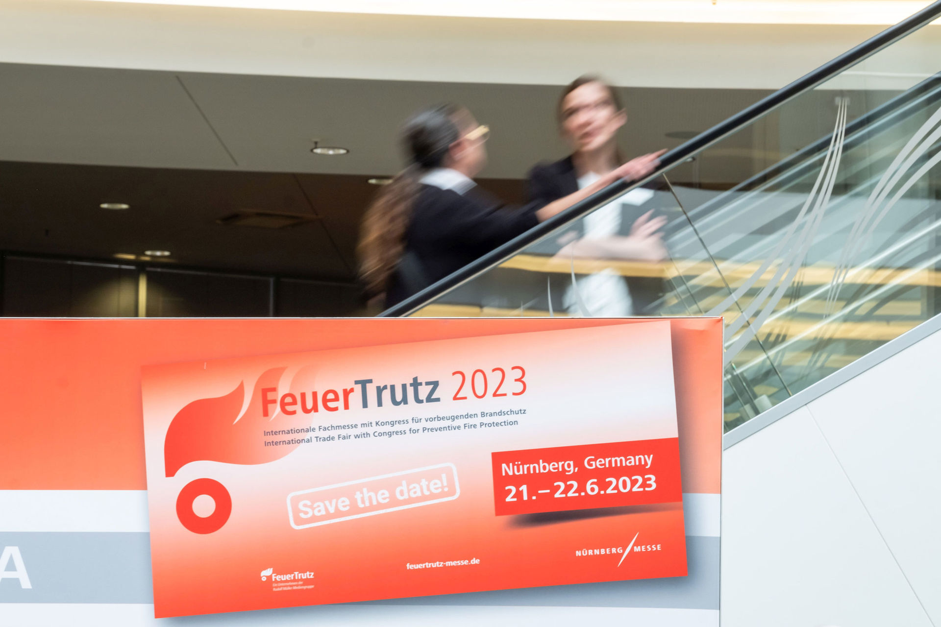 Besucher auf der FeuerTrutz hinter einem Plakat der FeuerTrutz 2023