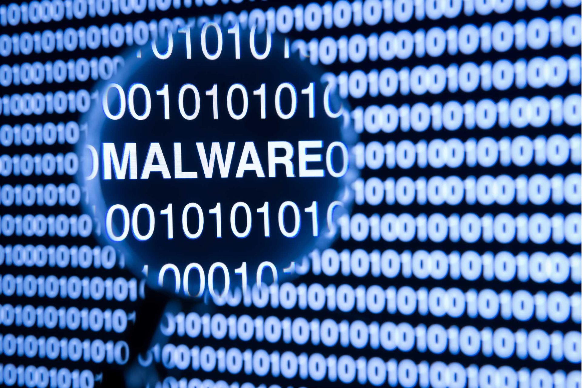Symbolbild: Binärcode, unter Lupenglas das Wort Malware