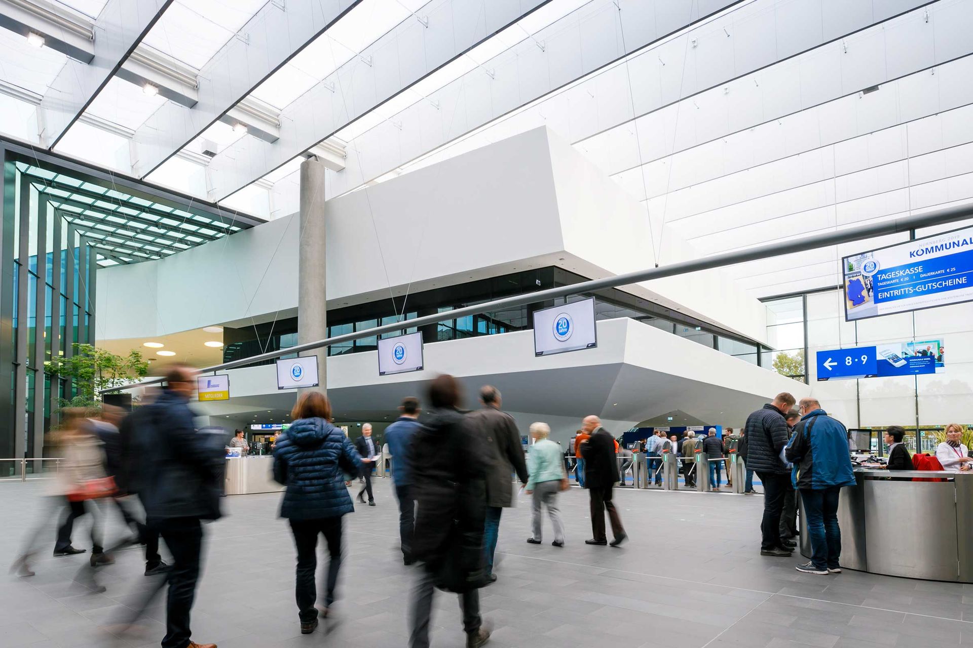 Das Bild zeigt den Eingang Mitte, Besucherinnen und Besucher strömen in Richtung Hallen.