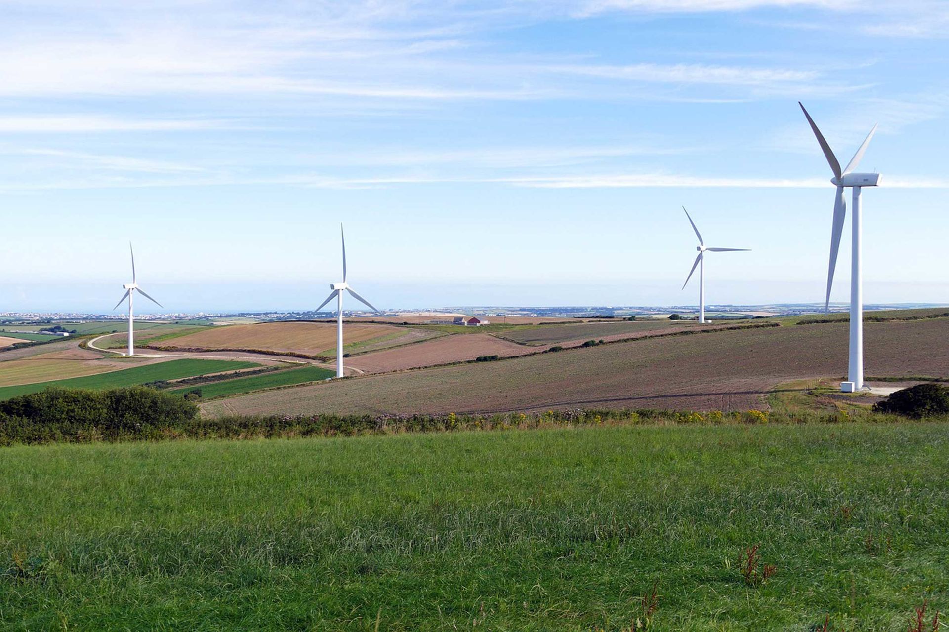 Das Bild zeigt Windkrafträder auf einem Feld und im Hintergrund Dörfer.