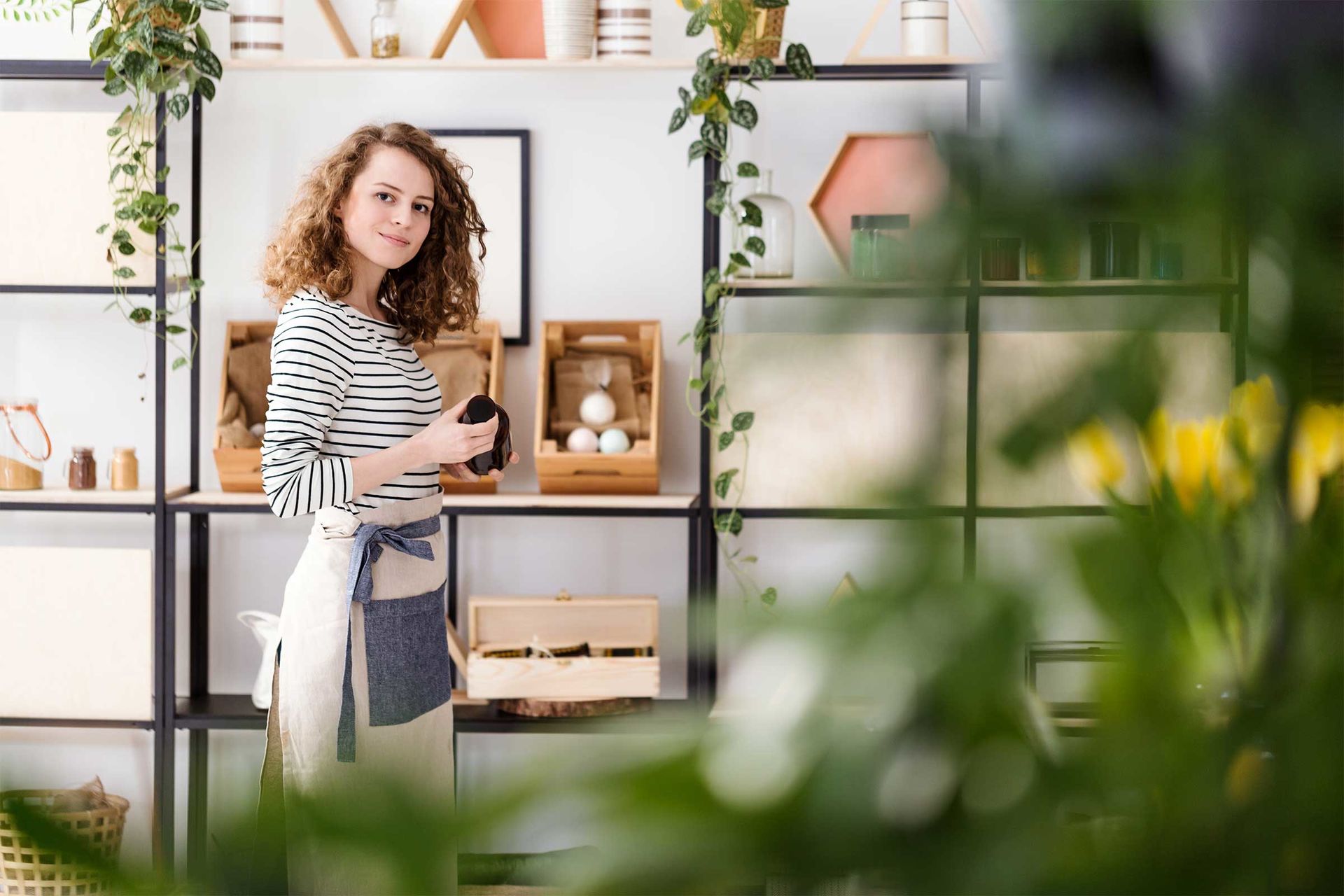 Deutsch Junge Frau mit Schürze vor Regal mit Naturkosmetik